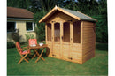 A wooden summerhouse with half-glazed double doors and arched top windows, situated on a grassy area with a small wooden table and chairs in front.