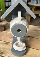 A gray teapot-shaped bird box with a beige base, designed to resemble a teapot with a bird entrance hole.