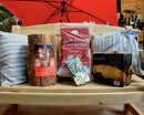 Kiln dried firewood packages and a log on a wooden surface with a red umbrella in the background.