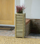 A wooden slatted square planter placed on a garden pathway, containing a pink flowering plant.